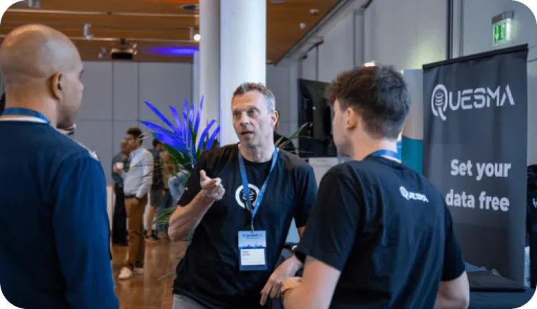 Three men talking at a tech event near a Quesma banner reading "Set your data free"