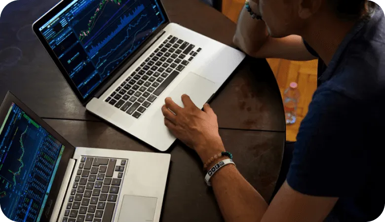 Person analyzing financial charts on 2 laptops at a wooden desk