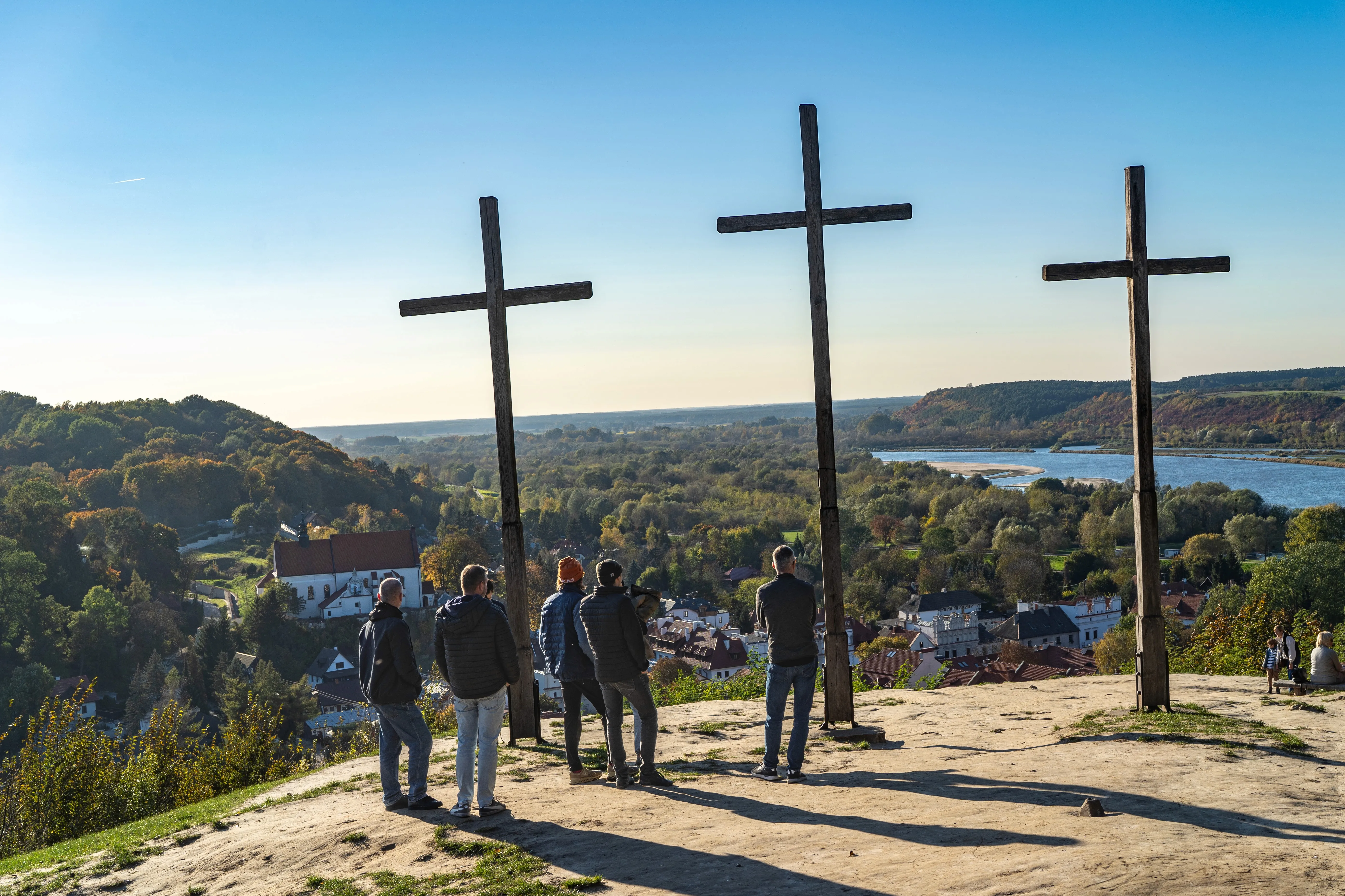 People standing by three large wooden crosses overlooking a scenic river valley