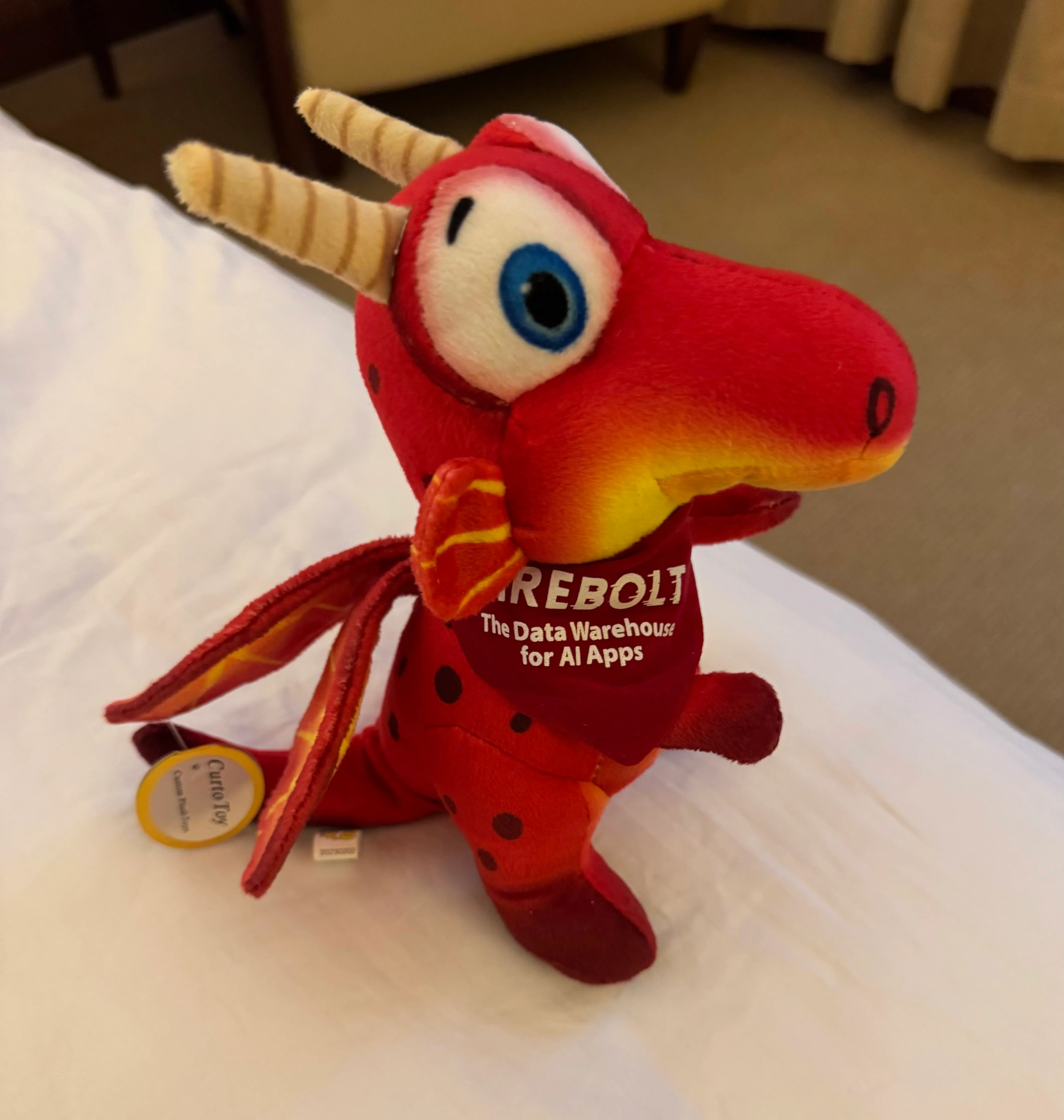 Plush red dragon toy with horns wearing a Firebolt shirt on a bed
