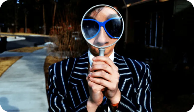 Person in striped suit holding magnifying glass up to their face outdoors